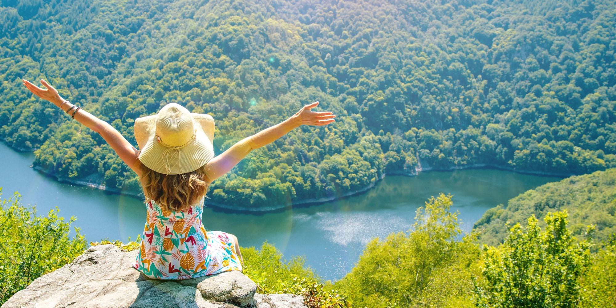 A woman wearing a hat sitting by a beautiful river